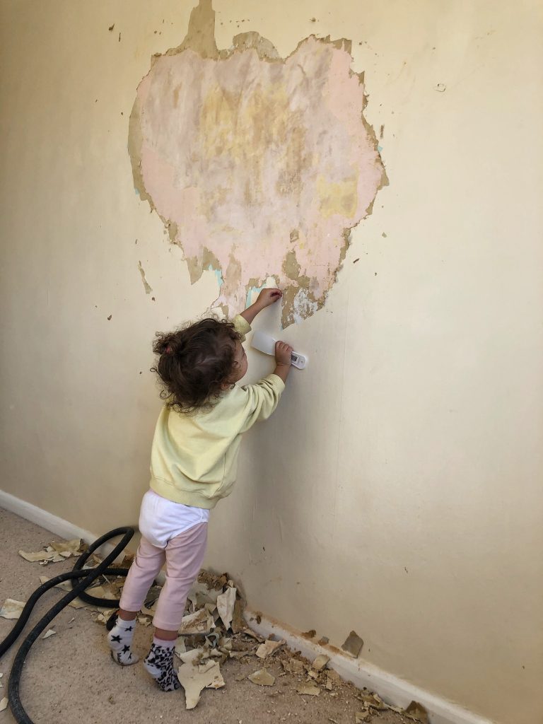 Image of a toddler helping to remove wallpaper in a bedroom.